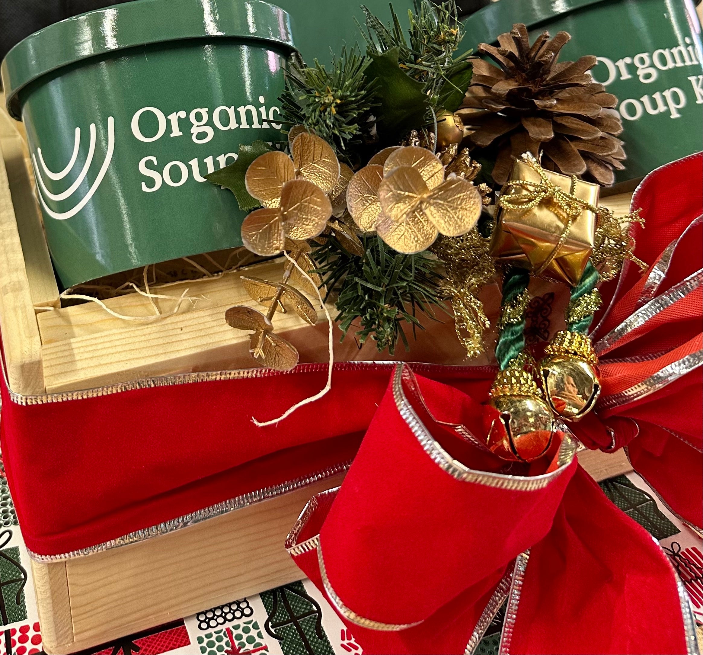 Organic Soup Kitchen soup gift box with evergreen sprigs, gold ornaments, and a red ribbon